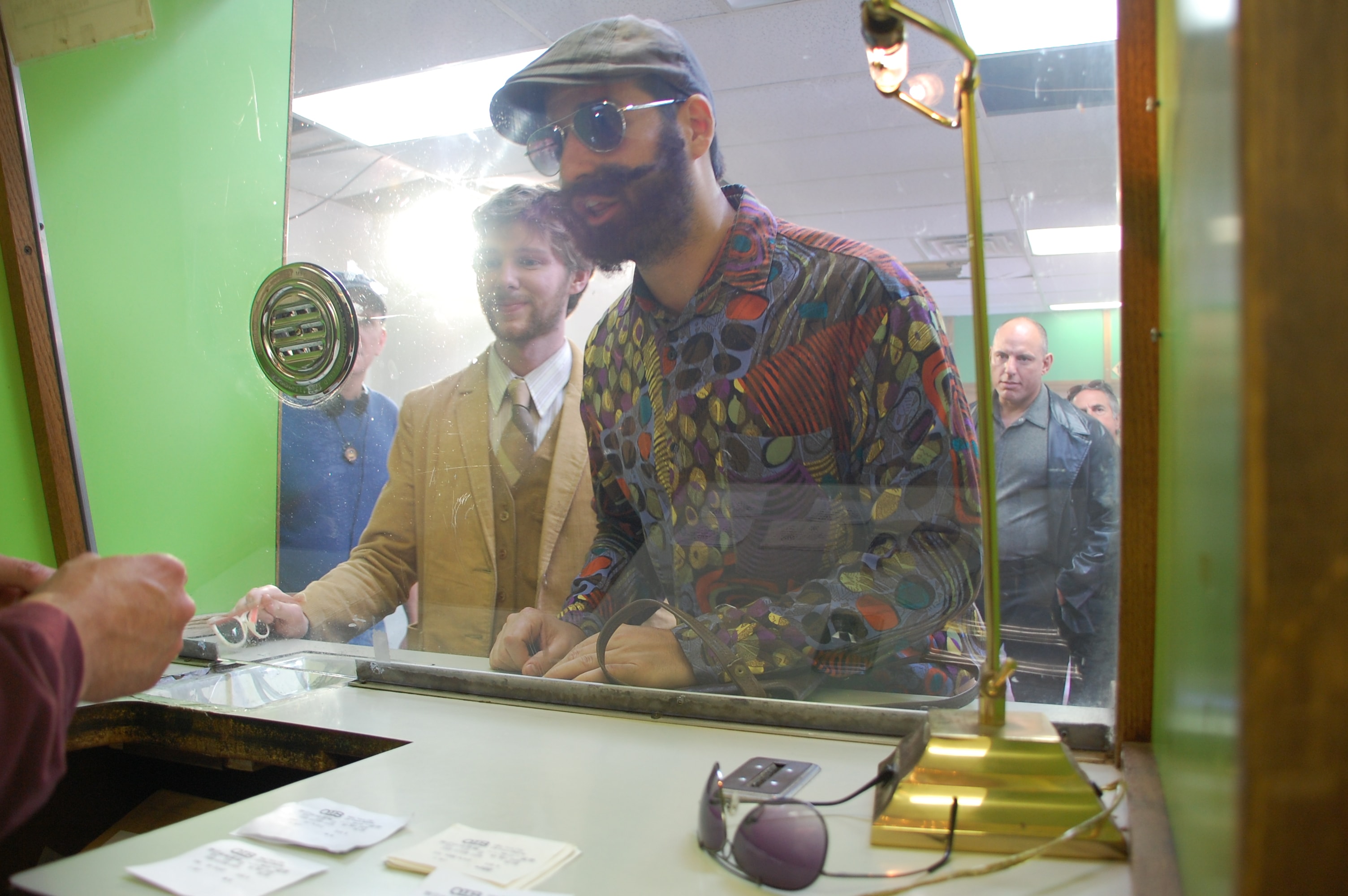 A bearded man in a colorful shirt leans through a pawn shop window