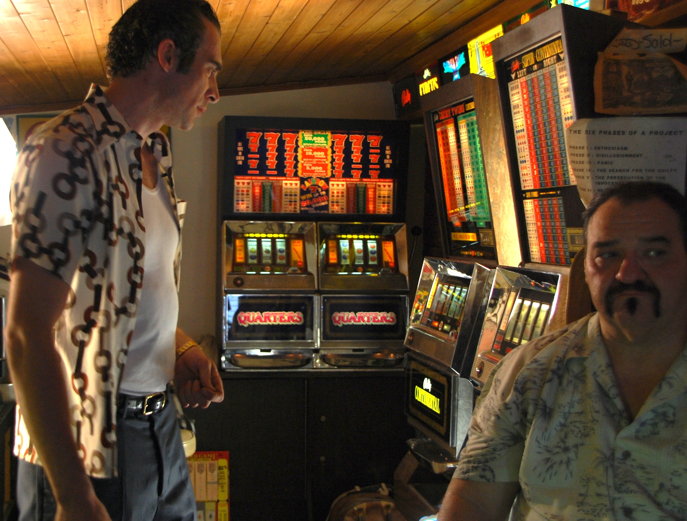 Two men among vintage slot machines in a dimly lit room
