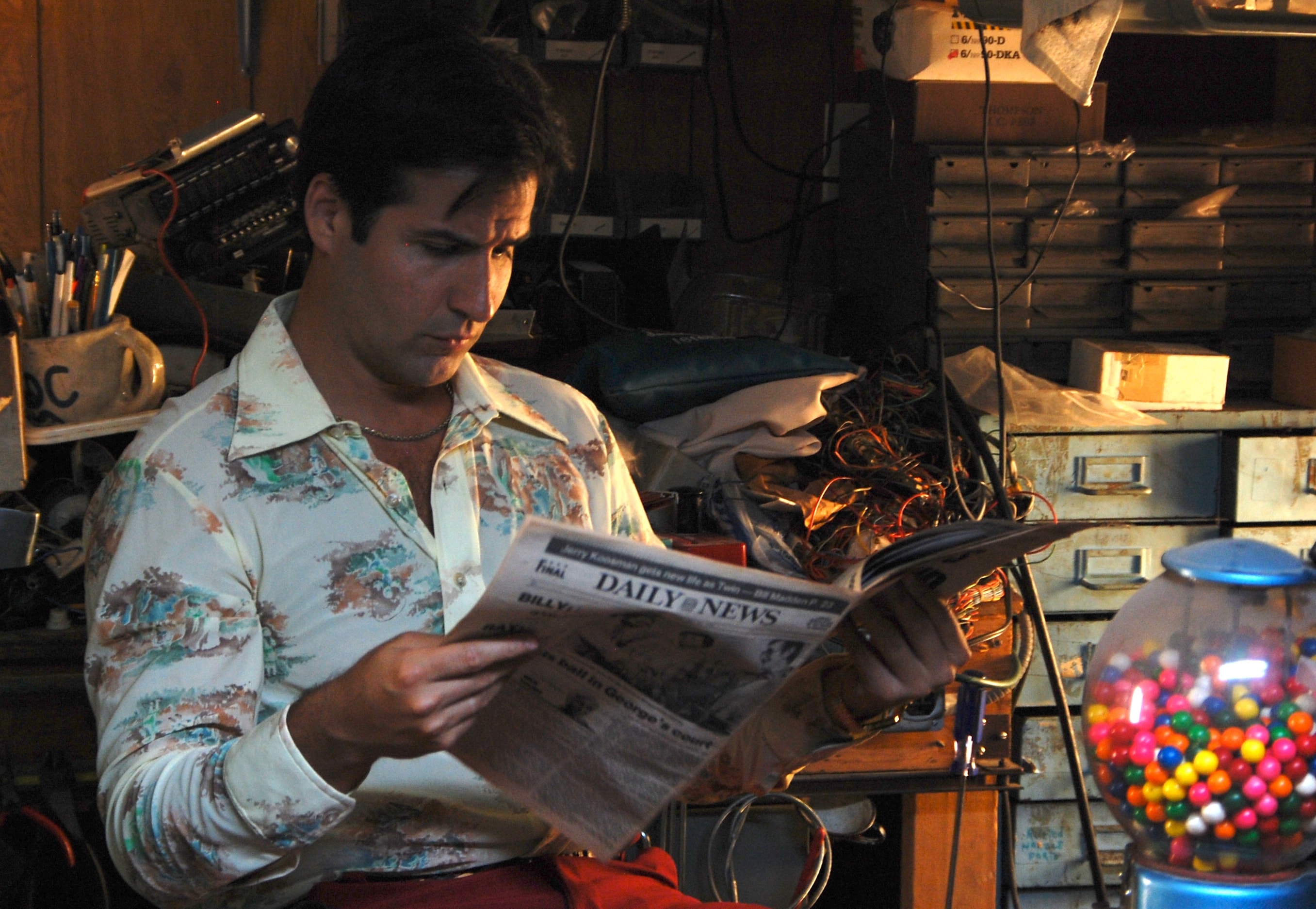 A man in a retro floral shirt reads the Daily News in a workshop