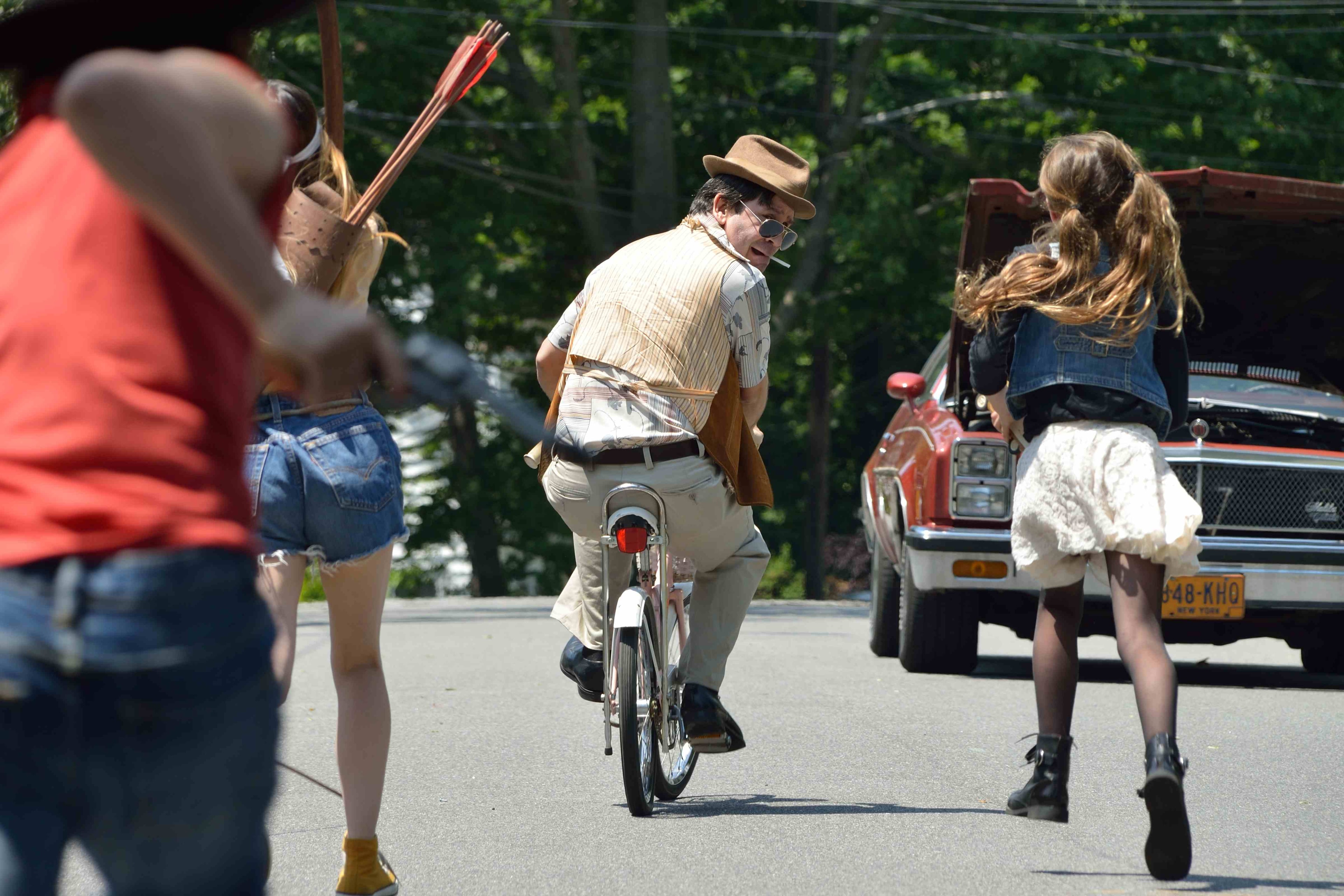A man in a hat rides a bicycle on a sunny suburban street
