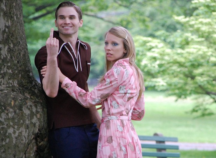 Two men in 1970s clothing stand outdoors in conversation